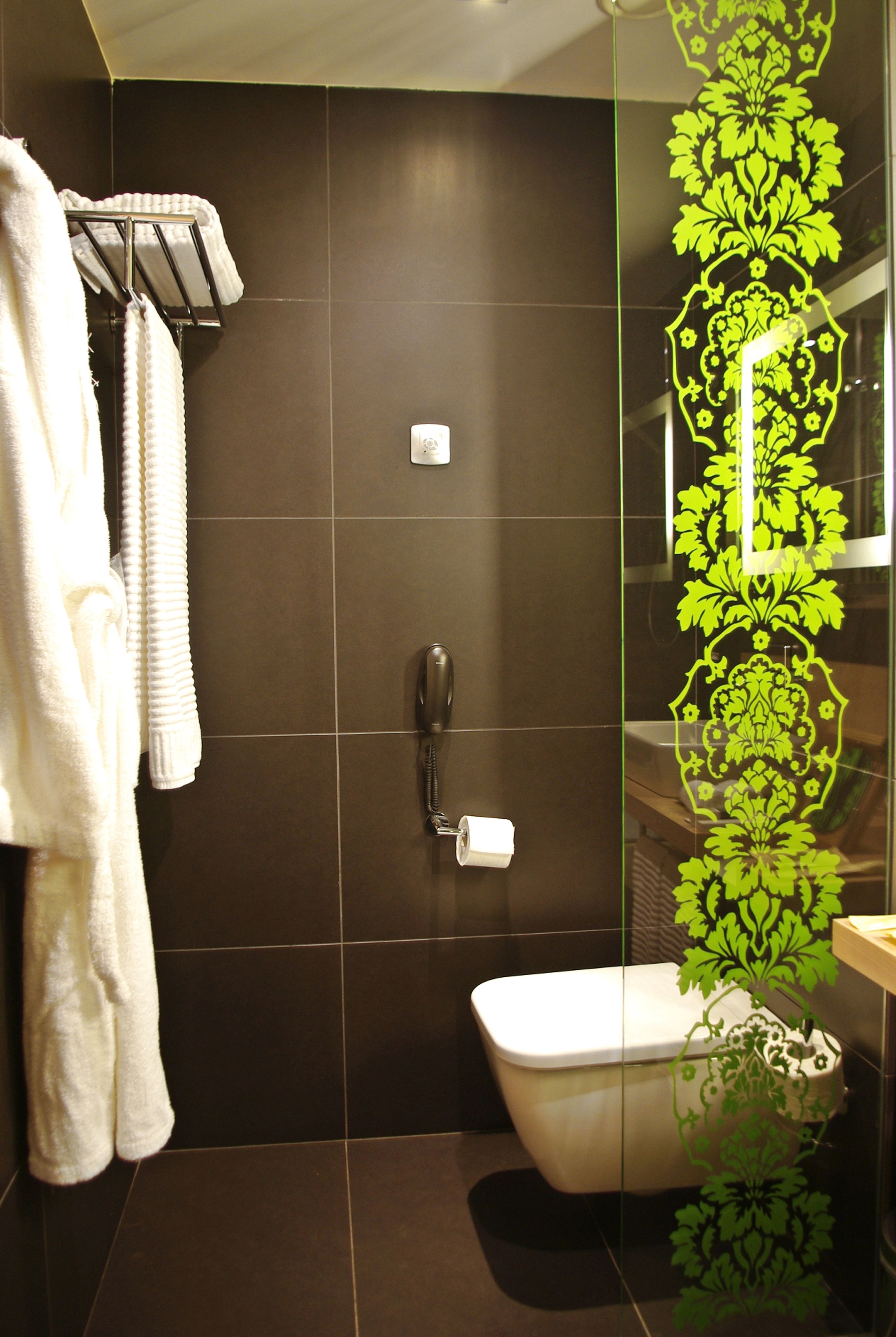 A modern bathroom with a toilet, a towel rack with towels, and a glass partition with a green decorative pattern.