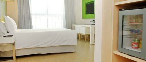 A hotel room with a bed, a desk, a television, and a minibar.