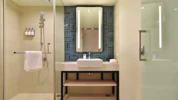 A modern bathroom with a glass shower enclosure, a white sink, and a large mirror above it.