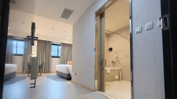A modern hotel room with a large bed, a desk, and a glass-enclosed shower area.