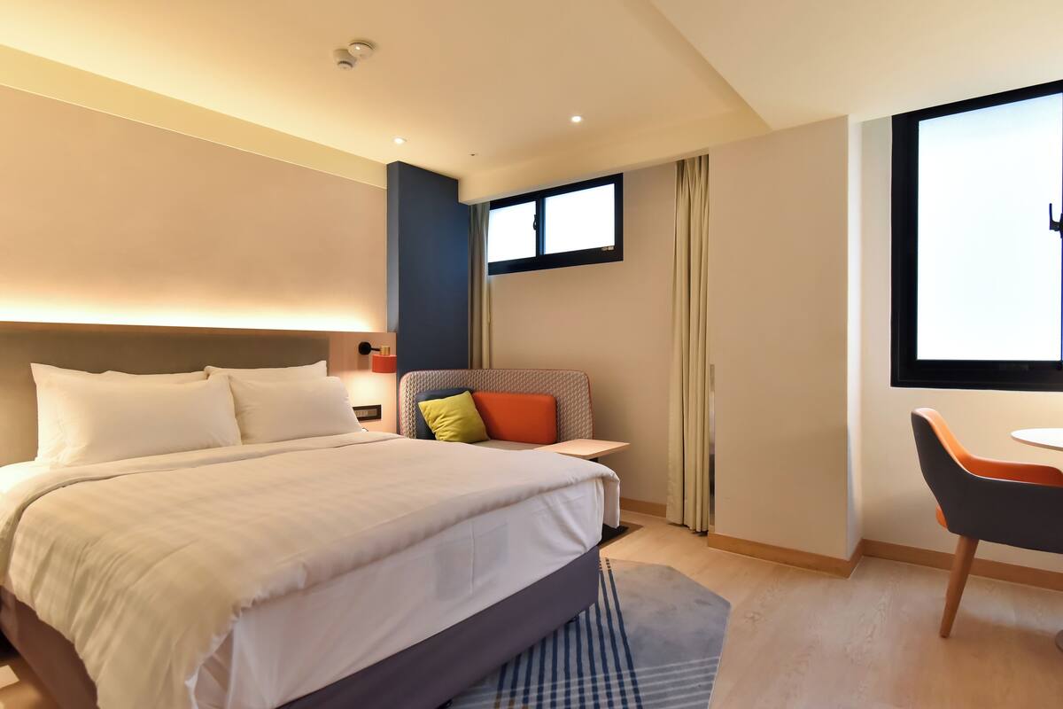 Habitación de hotel con una cama grande, un escritorio, una silla, una ventana y una puerta.