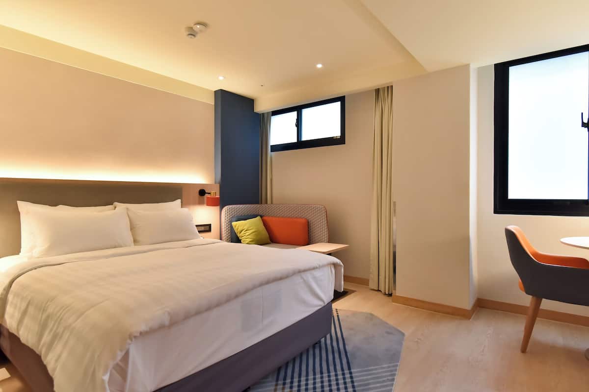 Habitación de hotel con una cama grande, un escritorio, una silla, una ventana y una puerta.