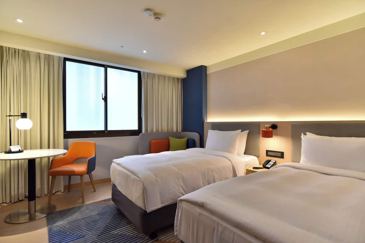 Een hotelkamer met twee bedden, een bureau en een stoel.