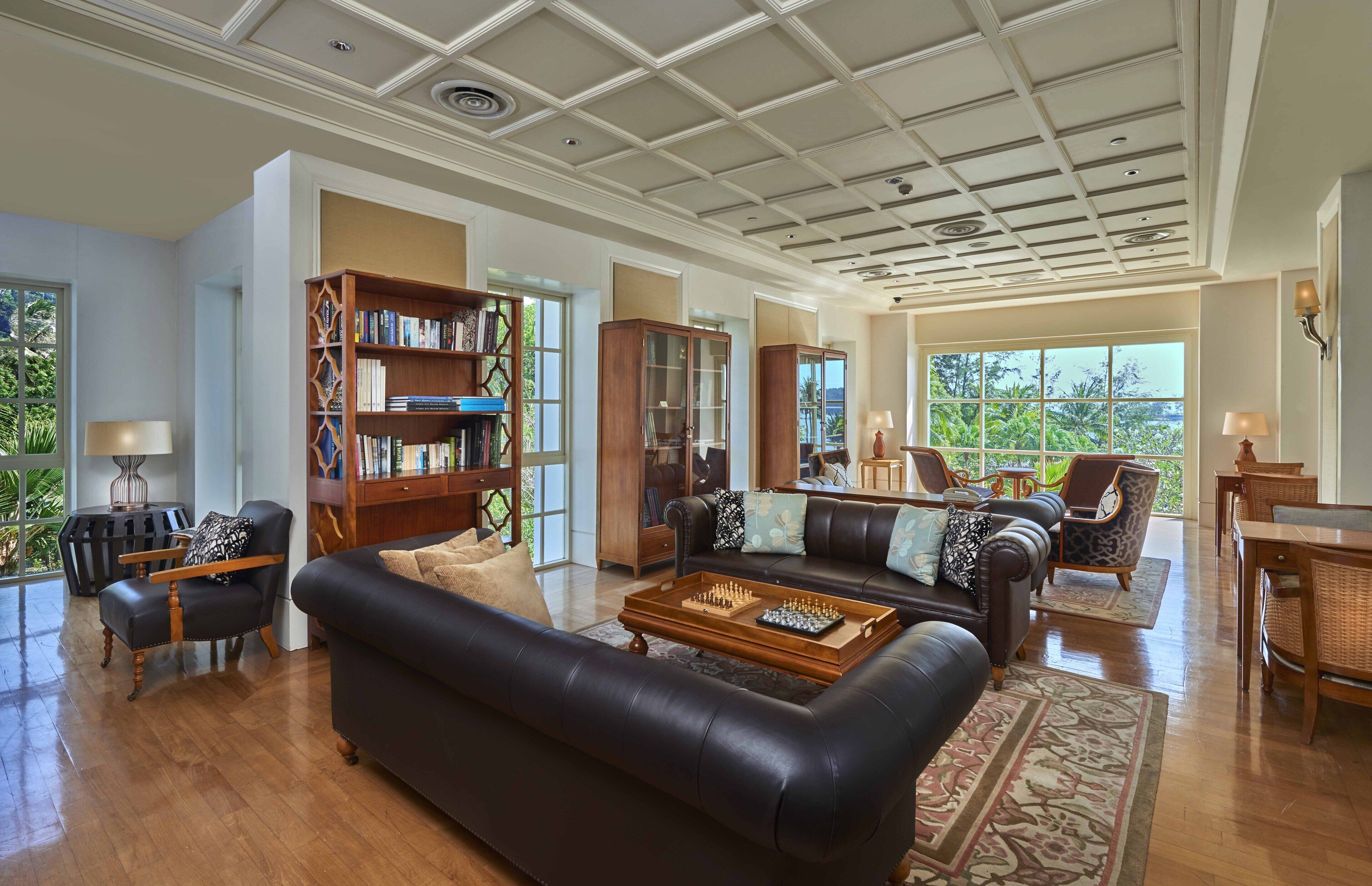 A spacious living room with a black leather sofa, a wooden coffee table, and a bookshelf.