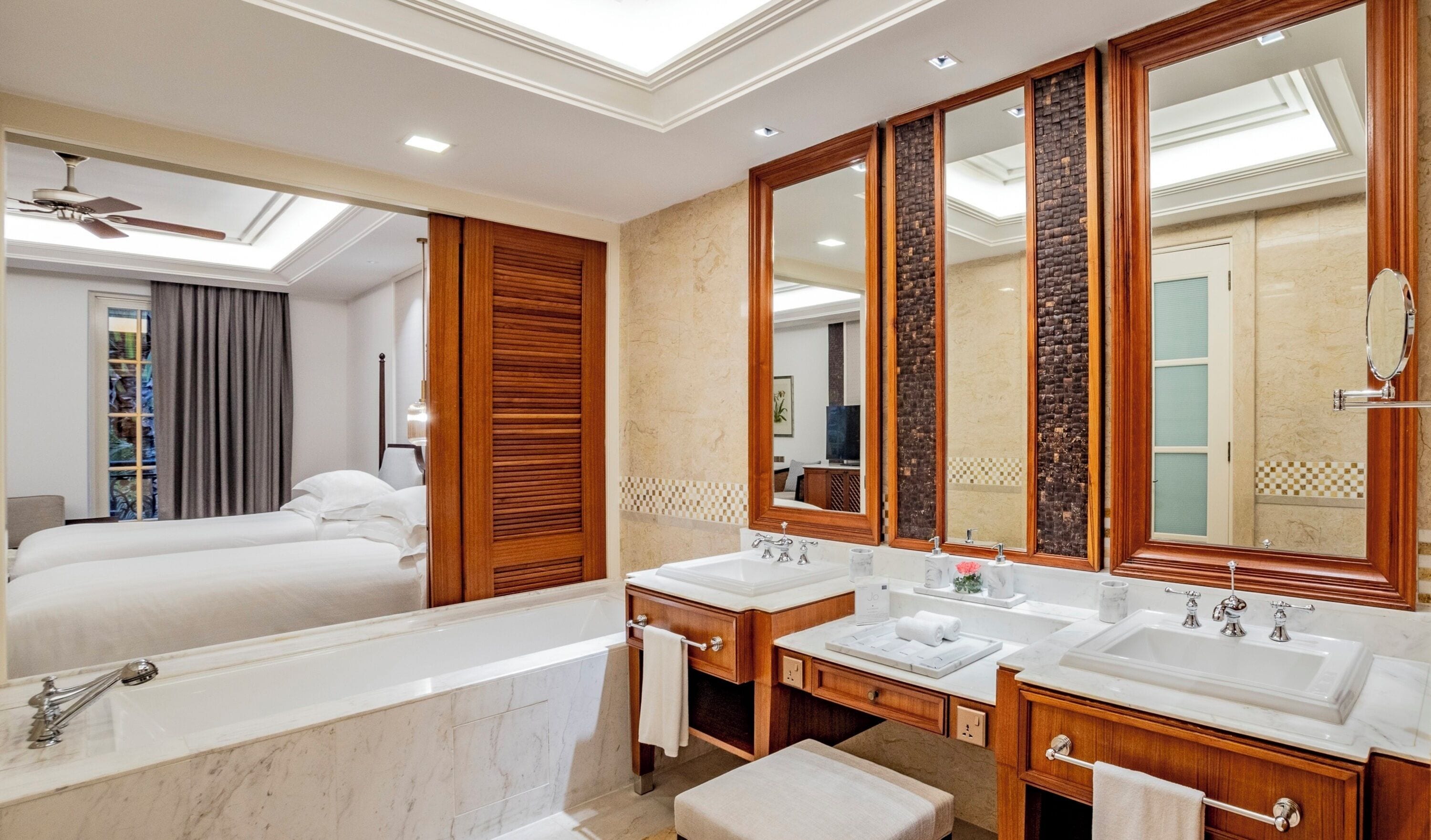 A hotel bathroom with a large mirror, two sinks, a bathtub, and a ceiling fan.