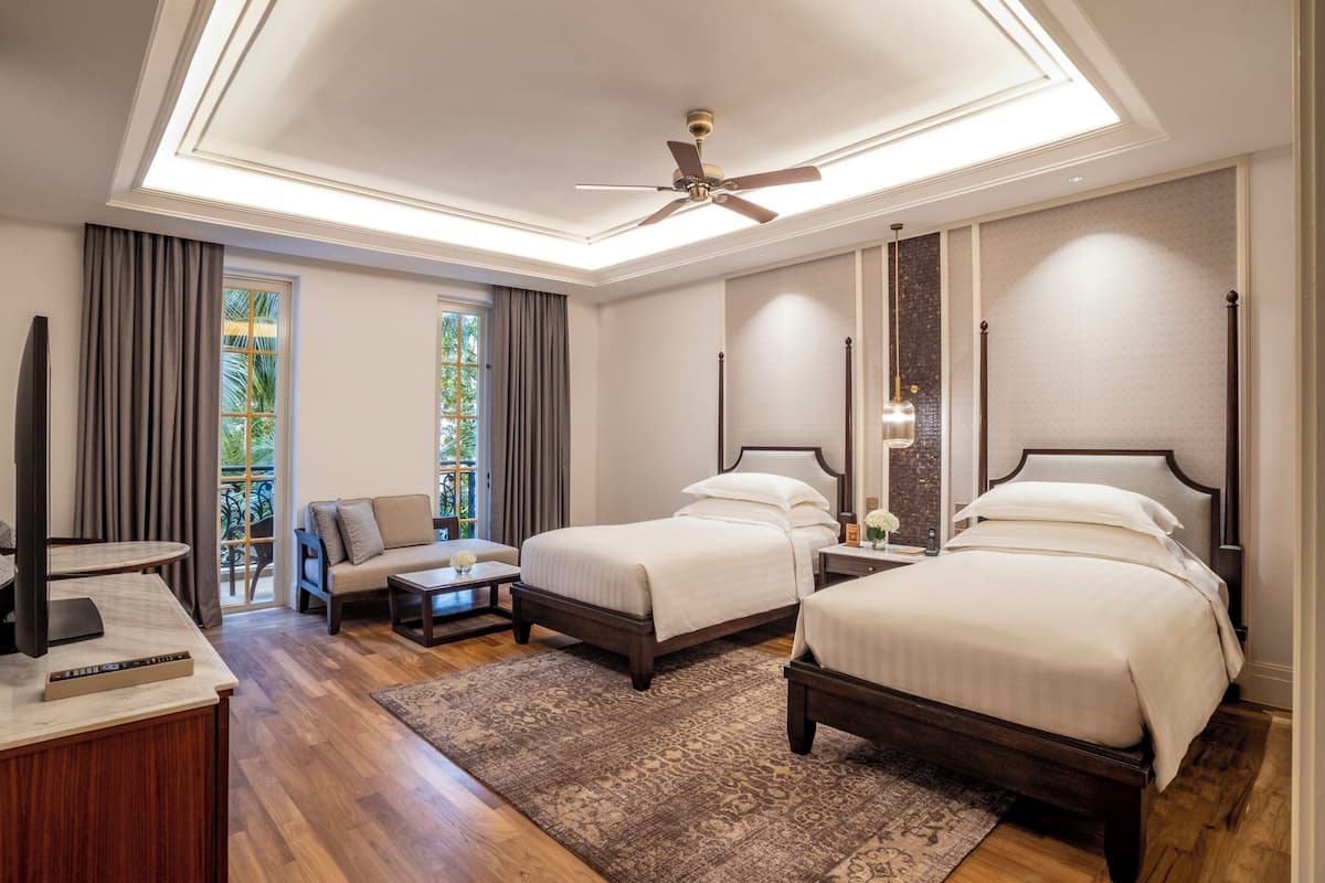 A hotel room with two beds, a desk, a chair, and a large window with curtains.