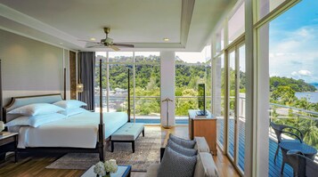 Ein geräumiges Schlafzimmer mit einem großen Bett, einem Schreibtisch und Blick auf eine üppige Landschaft durch große Fenster.