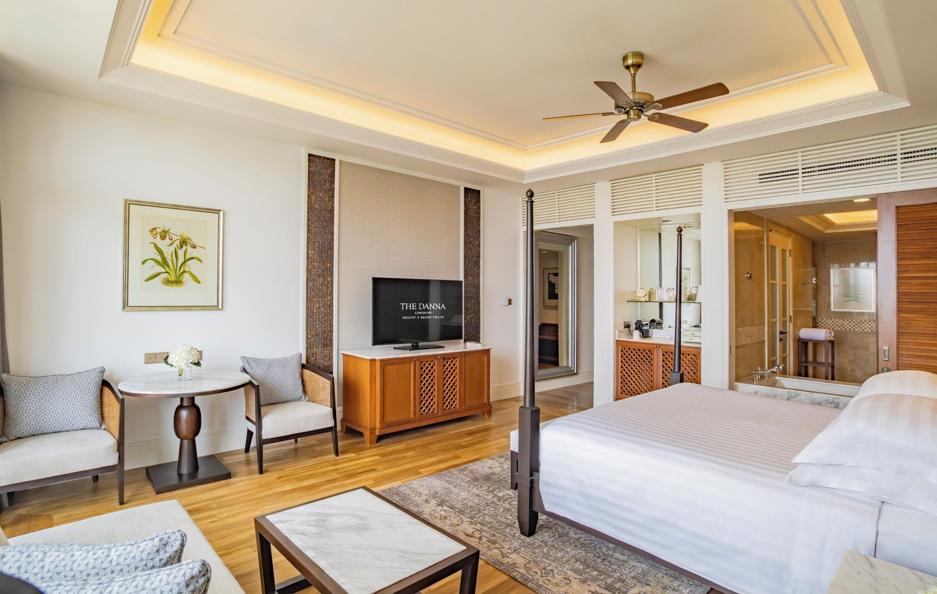 A hotel room with a large bed, a TV, a sofa, a small table, and a ceiling fan.