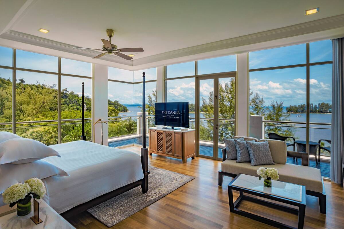 A spacious bedroom with a large bed, a television, and a balcony with a view of the water.