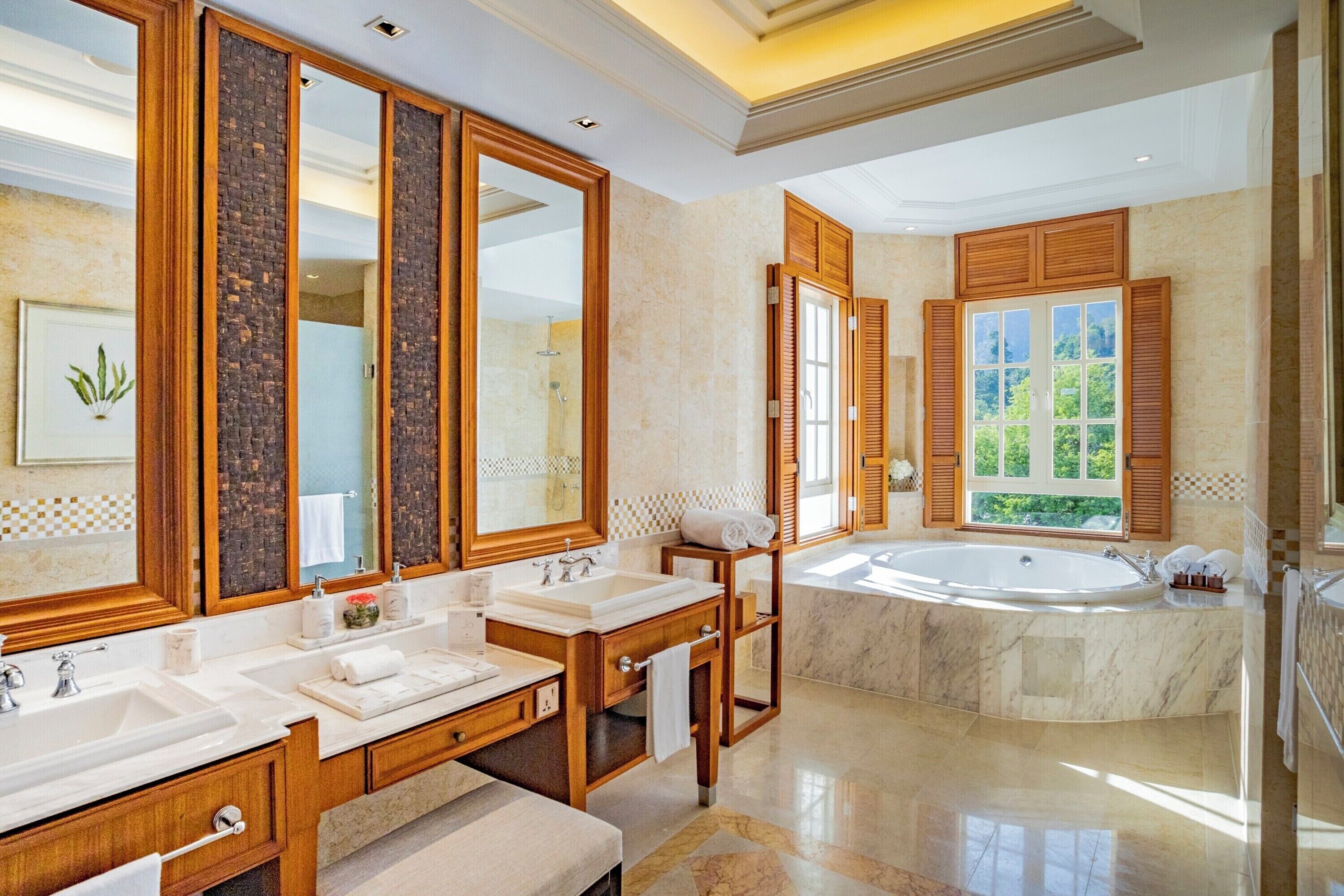 Ein luxuriöses Badezimmer mit zwei Waschbecken, einem großen Spiegel, einer Badewanne und einem Fenster mit Blick auf Grünfläche.