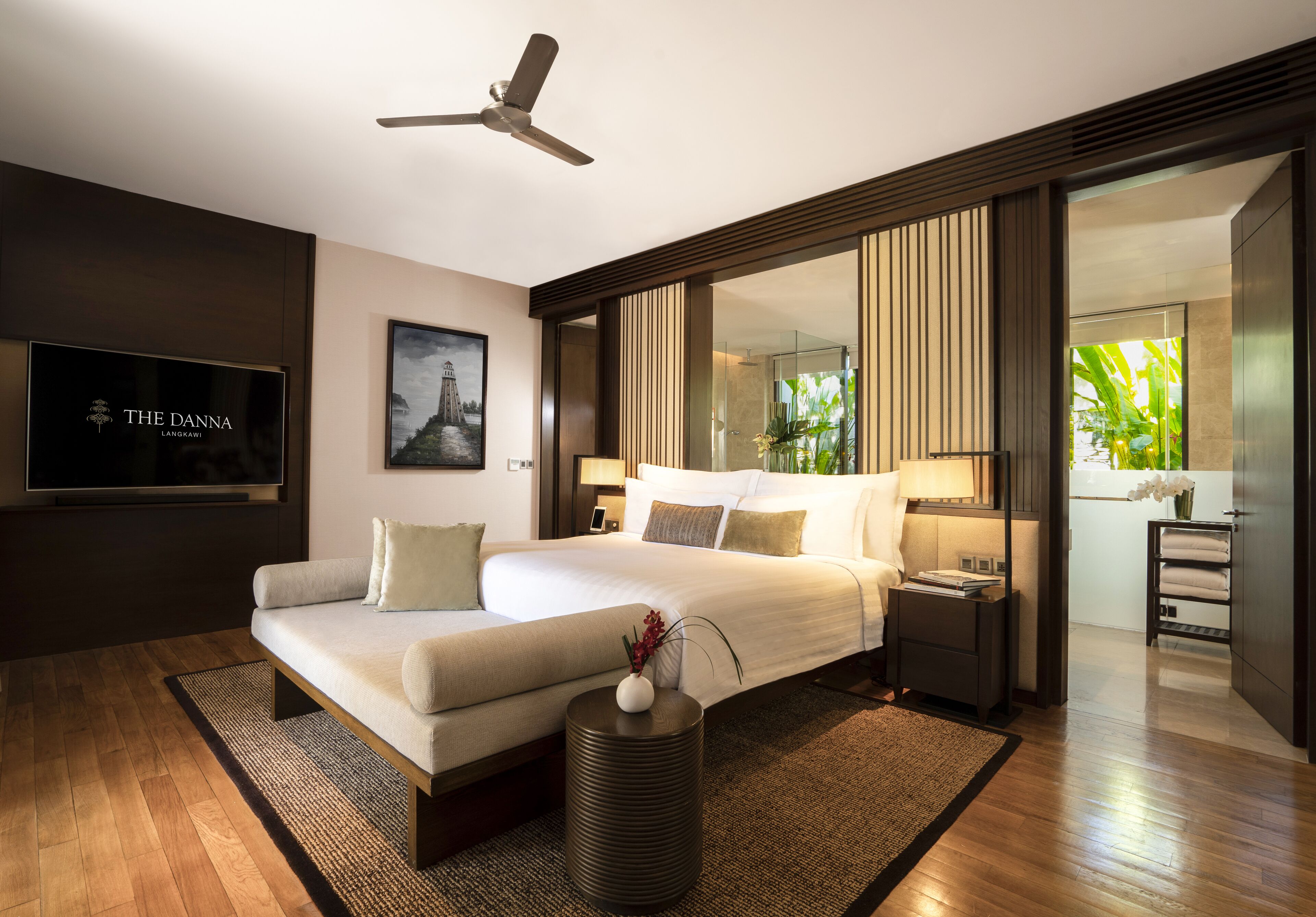 A modern hotel room with a large bed, a flat-screen TV, a ceiling fan, and a view of the garden.