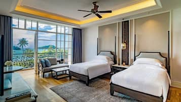 A hotel room with two beds, a desk, a chair, a ceiling fan, and a view of the ocean.