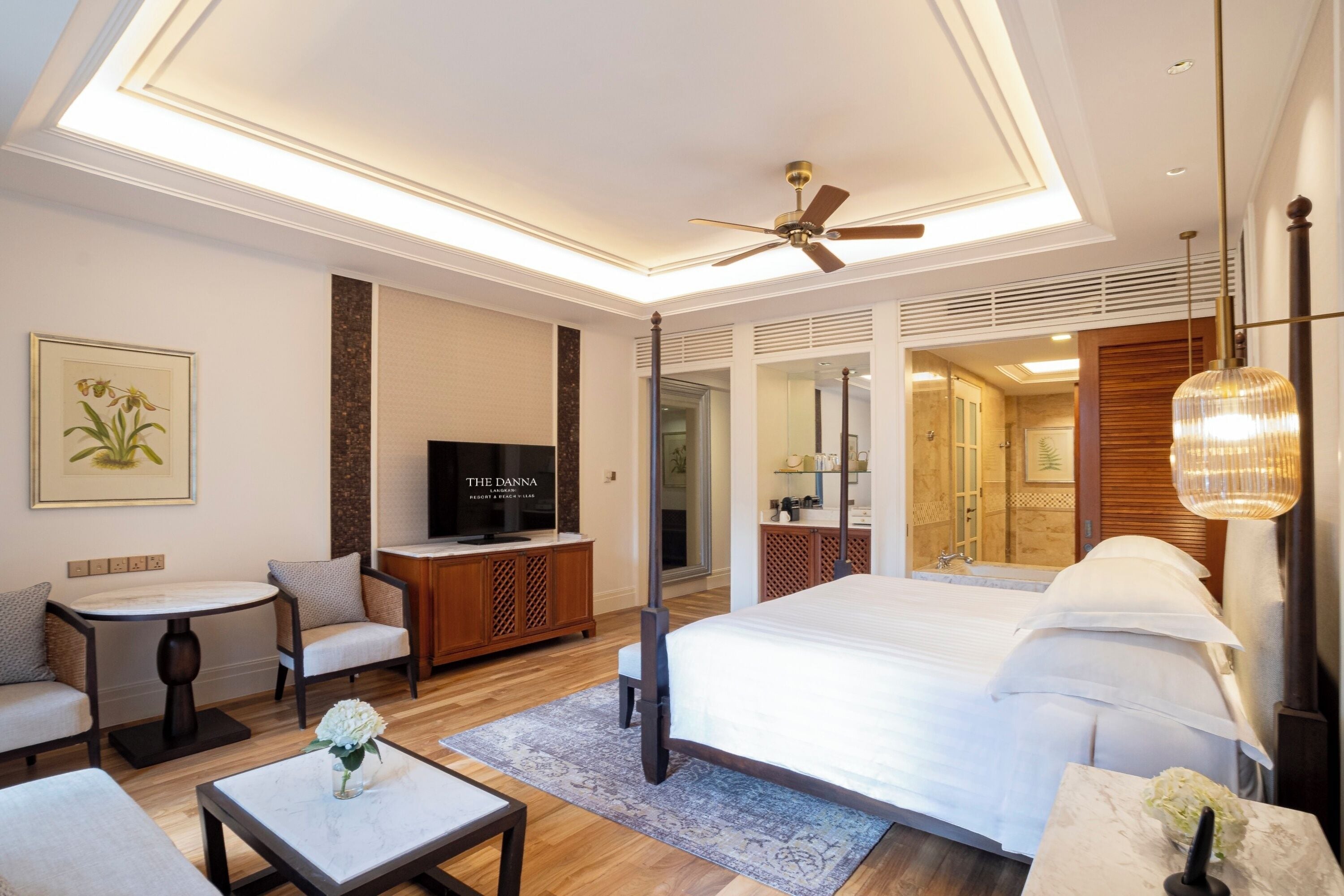 A modern hotel room with a large bed, a television, a seating area with chairs, and a small table with a vase.