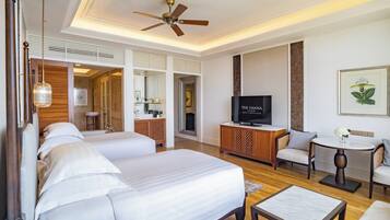 Habitación de hotel con una cama grande, televisor, zona de estar con sillas, una mesita y un ventilador de techo.