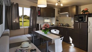 A modern kitchen with a dining area, featuring a large window, dark wooden cabinets, a white refrigerator, and a dining table with chairs.