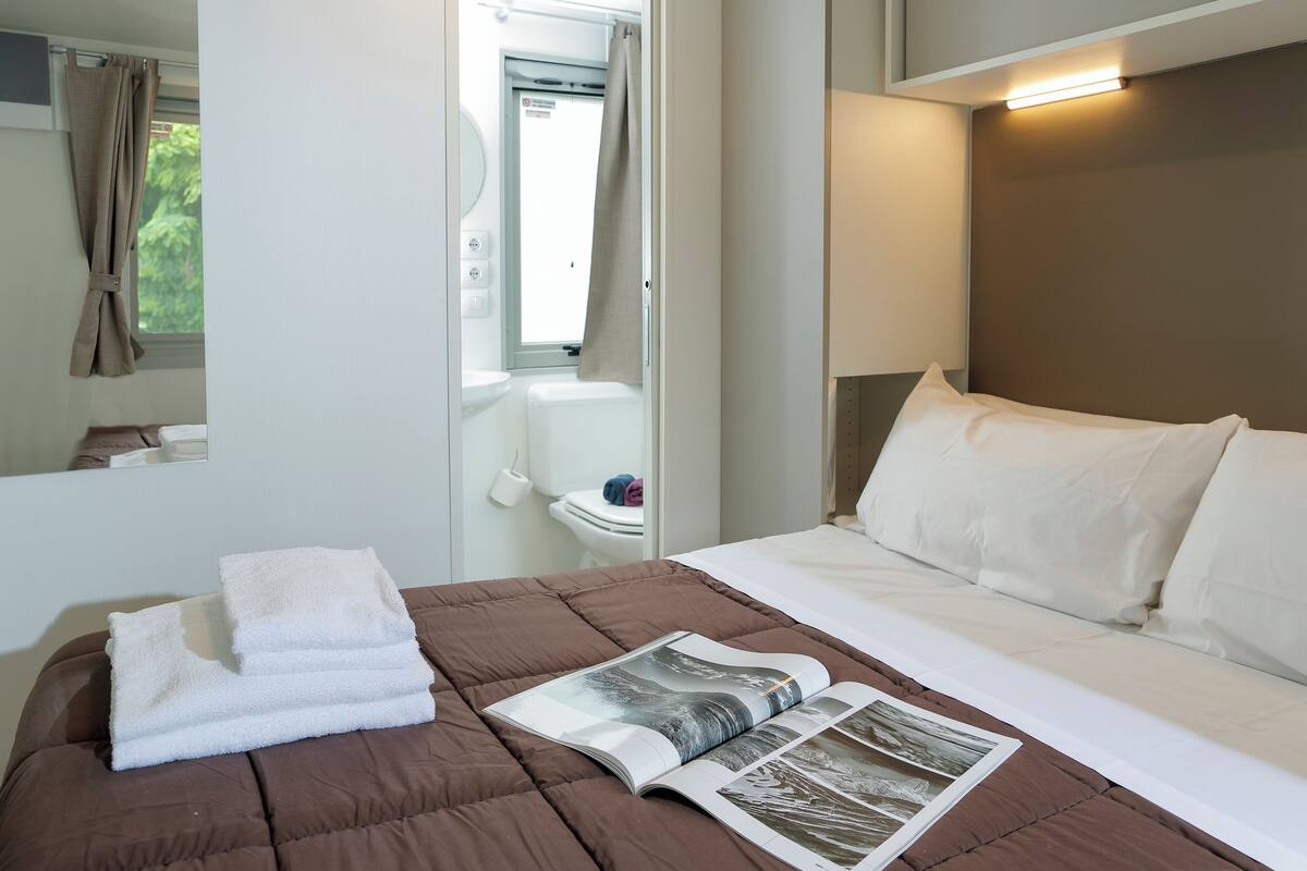 A neatly made bed with white linens, a brown bedspread, and a magazine on the bed.