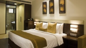 A hotel room with a large bed, a bedside table with a lamp, and a wall-mounted artwork. - Shervani Hotel Nehru Place (New Delhi)