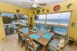 A dining area with a view of the beach, wooden furniture, and decorative wall art. - Coral Stone Club (Seven Mile Beach)