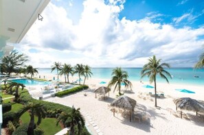 A beach view with a pool, palm trees, and beach umbrellas. - Coral Stone Club (Seven Mile Beach)