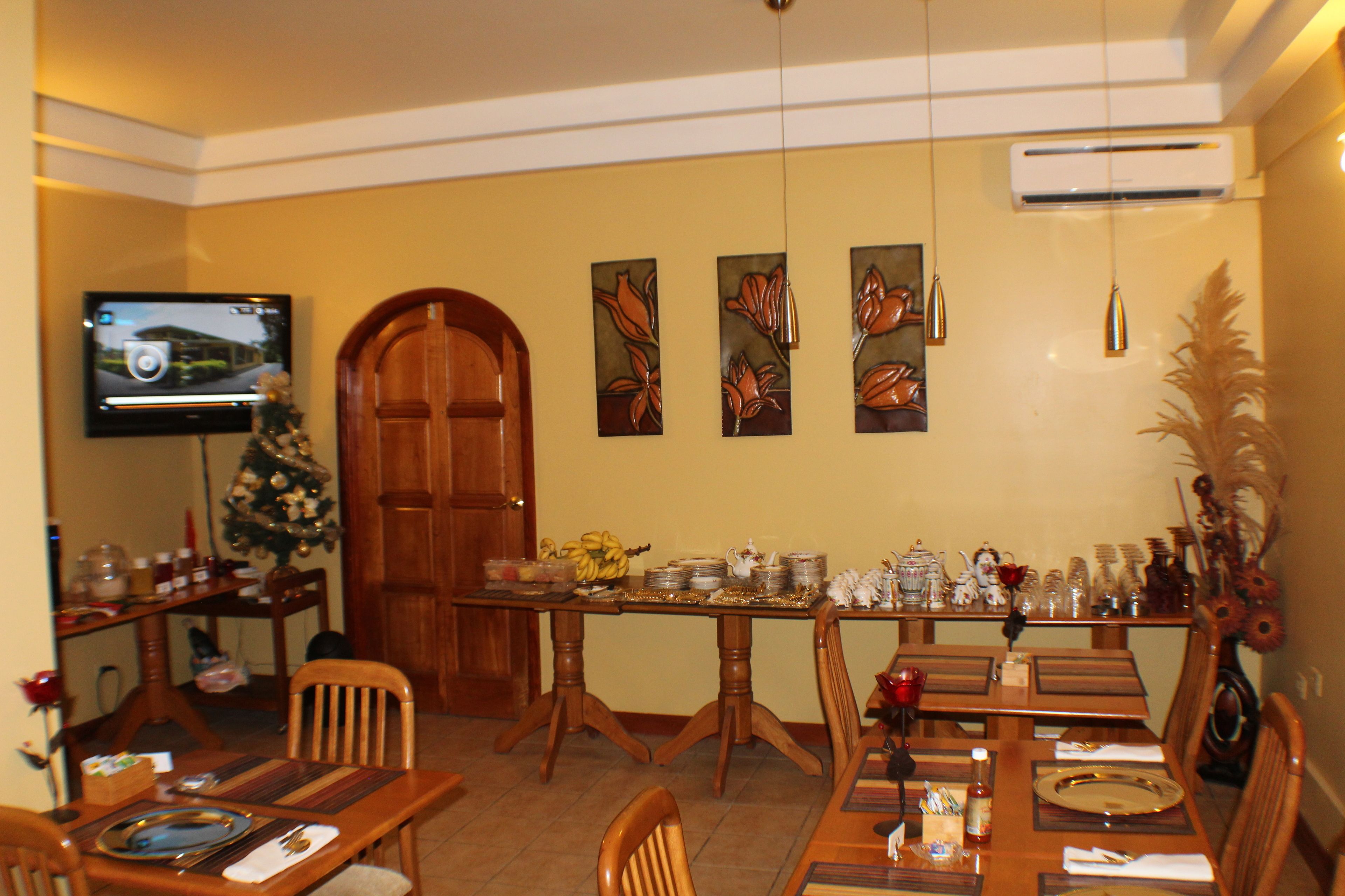 Un'area pranzo con un tavolo di legno apparecchiato per sei persone, un albero di Natale e una televisione appesa al muro.