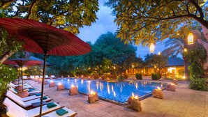 Un área junto a la piscina con sillones y sombrillas, rodeada de árboles y elementos de piedra.
