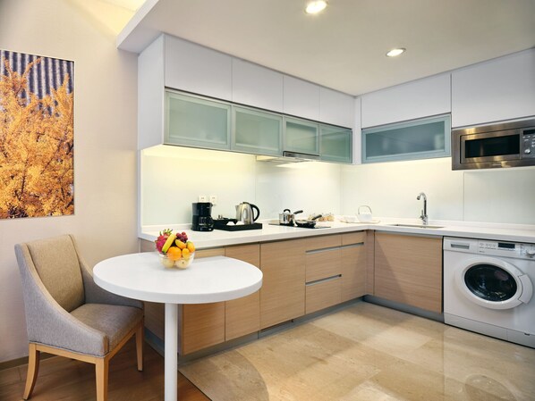Una cocina moderna con armarios blancos, microondas, cafetera y lavadora.