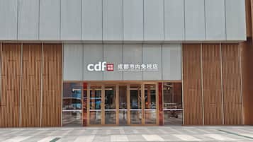 A modern building with a duty-free shop entrance, large glass doors, and a tiled pavement in front.