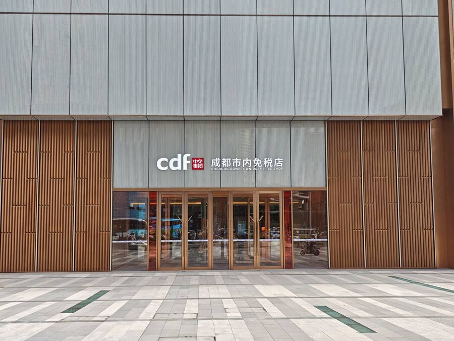 A modern building with a duty-free shop entrance, large glass doors, and a tiled pavement in front.