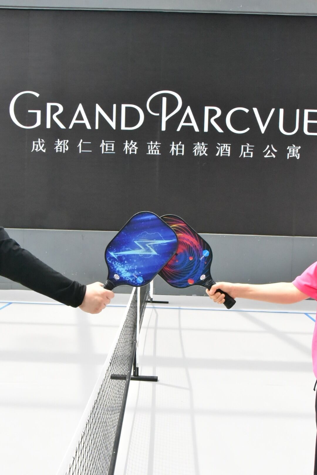 Two people holding paddles in front of a sign with the text 'GRAND PARC VUE'.