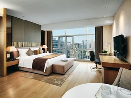 Una habitación de hotel moderna con una cama grande, un escritorio, una silla, un televisor y vistas de la ciudad.