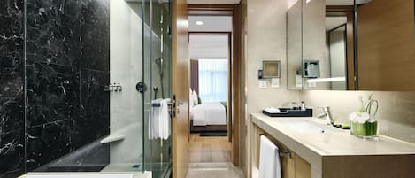 A modern hotel bathroom with a glass-enclosed shower, a large mirror, and a vanity with a sink and towel rack.