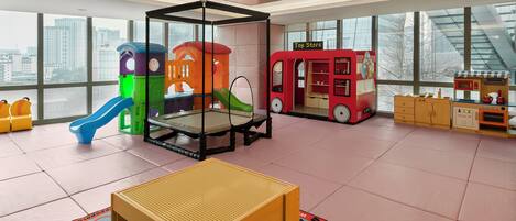 Un grand espace de jeux intérieur comprenant un trampoline, des structures de jeu et un magasin de jouets.