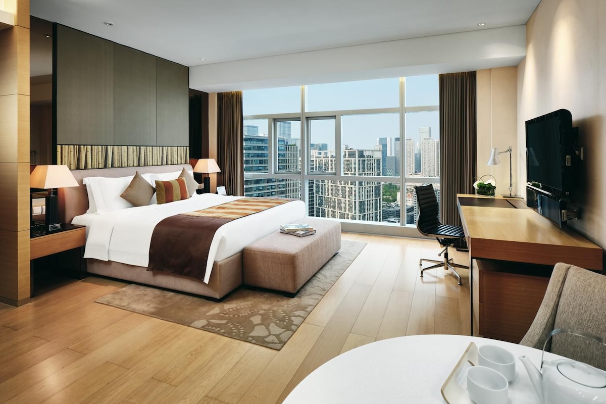 Una habitación de hotel moderna con una cama grande, un escritorio, un televisor y vistas a la ciudad.