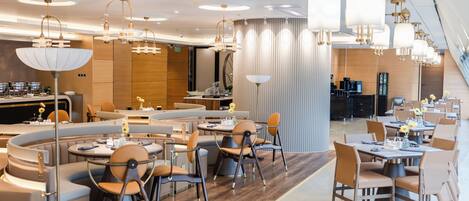 Un restaurante moderno con mesas redondas, asientos acolchados e iluminación colgante.