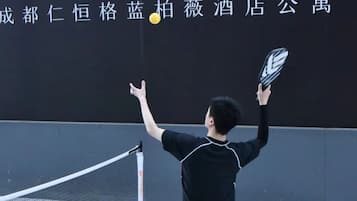 A tennis player in a black outfit on a tennis court with a net in the middle, and a sign with Chinese characters in the background.