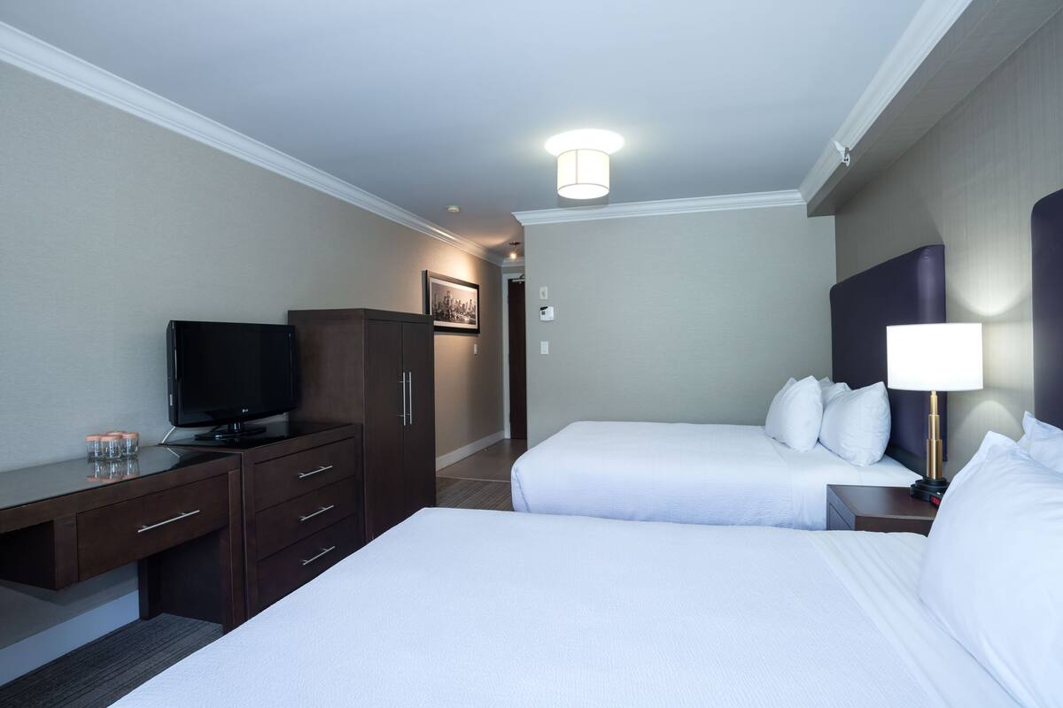 A hotel room with two beds, a desk with a television, a wardrobe, and a bedside lamp.