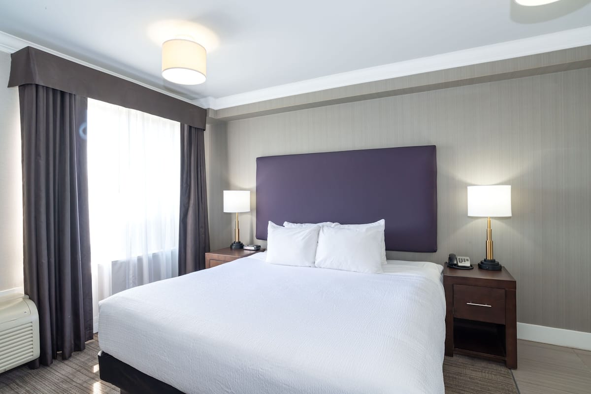 A hotel room with a large bed, two bedside tables with lamps, a heater, and a window with curtains.