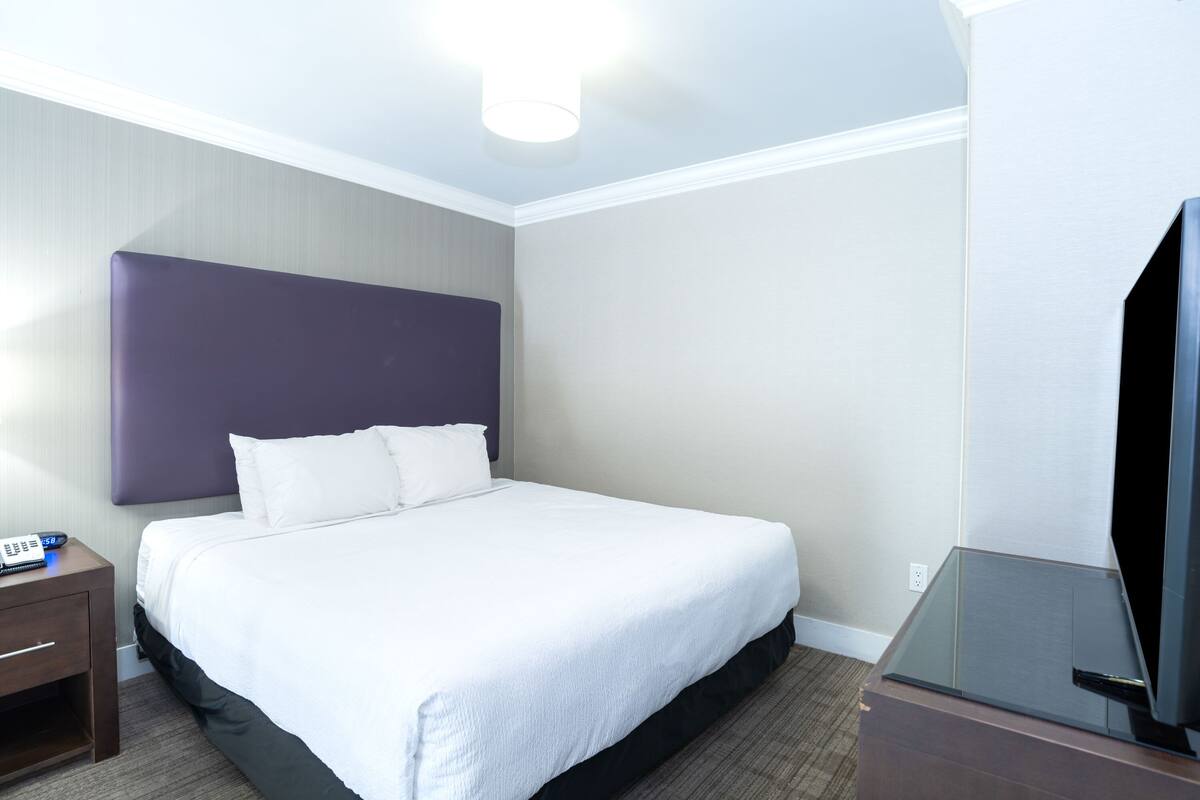 A hotel room with a large bed, a nightstand with a phone, and a TV on a stand.