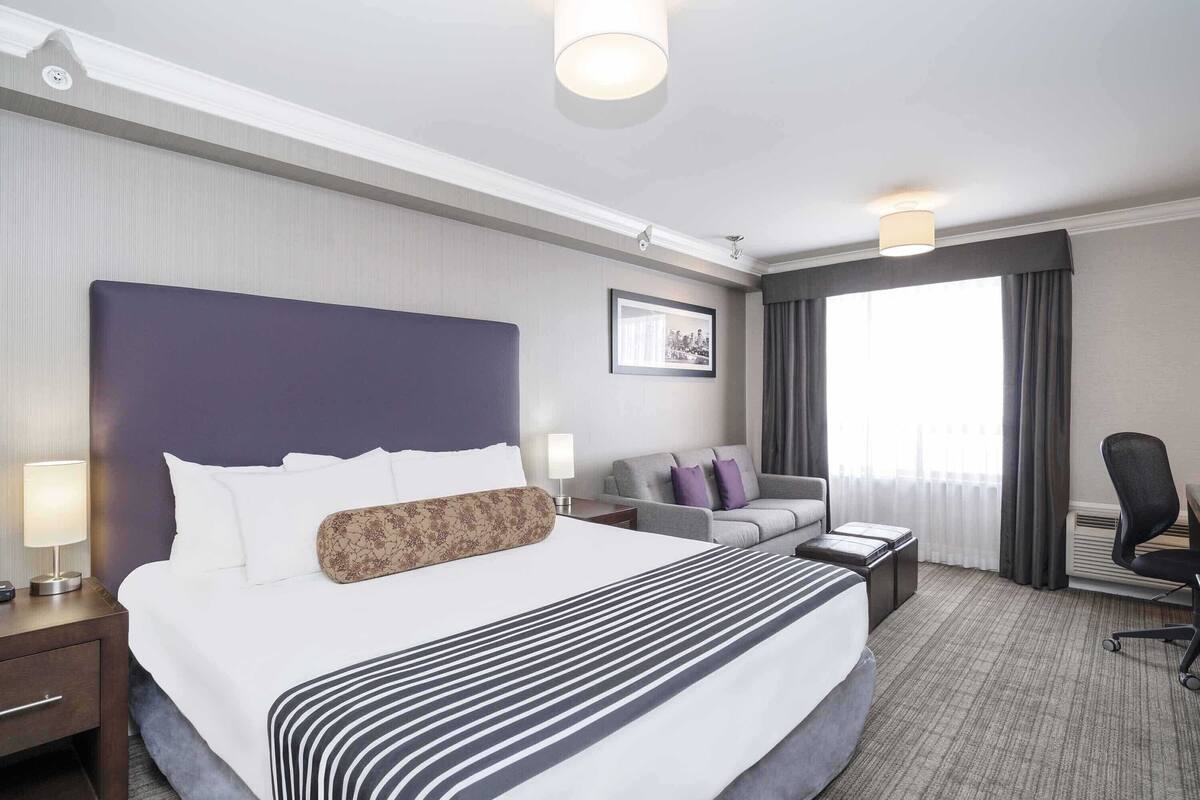 A hotel room with a large bed, a sofa, a desk, and a chair.