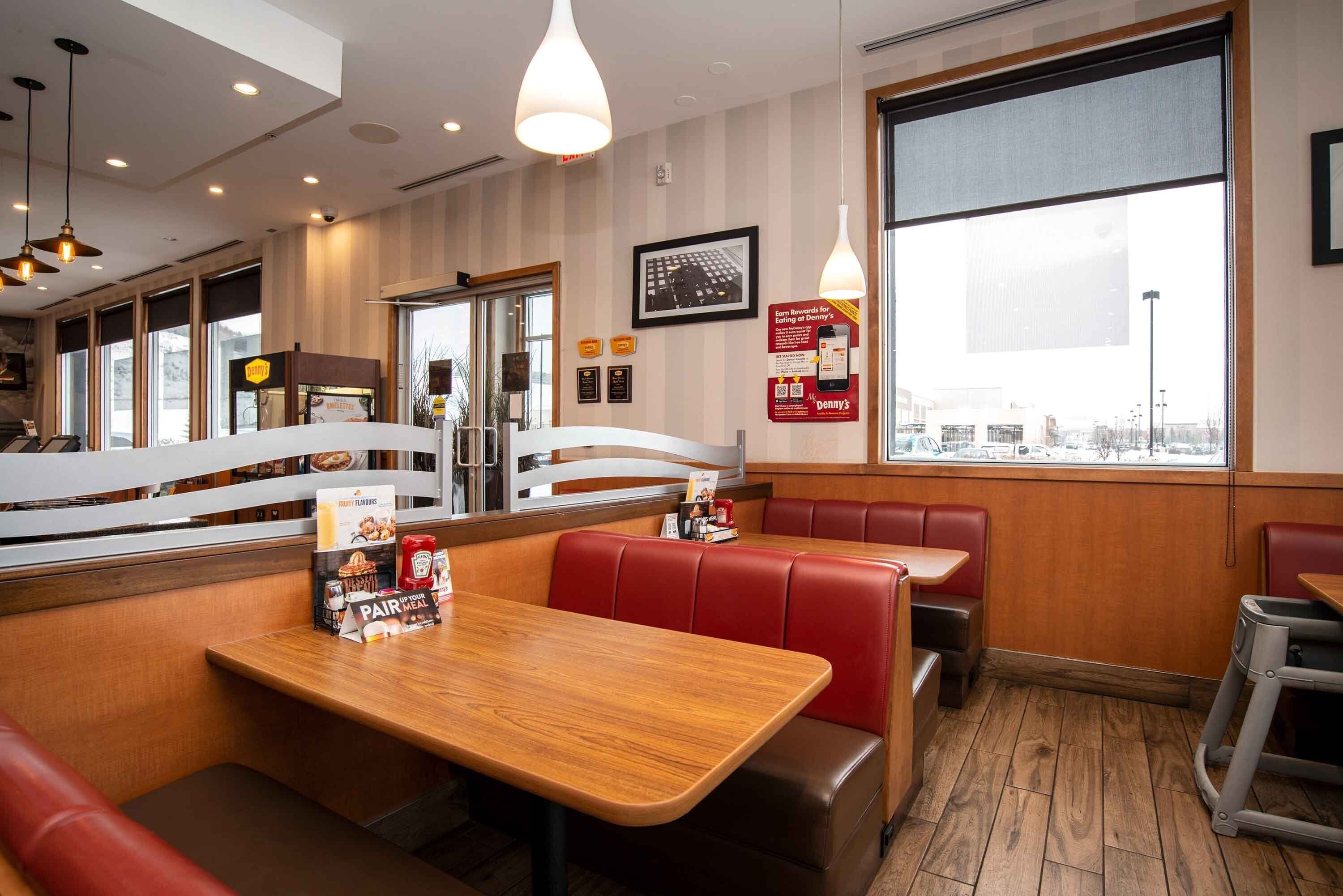 Un interior de restaurante con mesas de madera, cabinas de cuero rojo y ventanas amplias que ofrecen vistas al exterior.