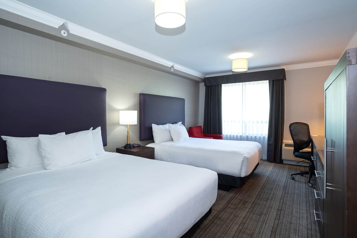 A hotel room with two beds, a desk, a chair, and a large window with curtains.