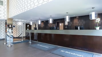 A hotel reception area with a modern design, including a reception desk, a patterned wall, and a geometric ceiling.