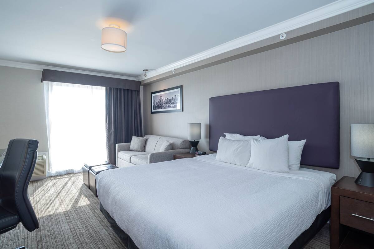 A hotel room with a large bed, a sofa, a desk, and a chair.
