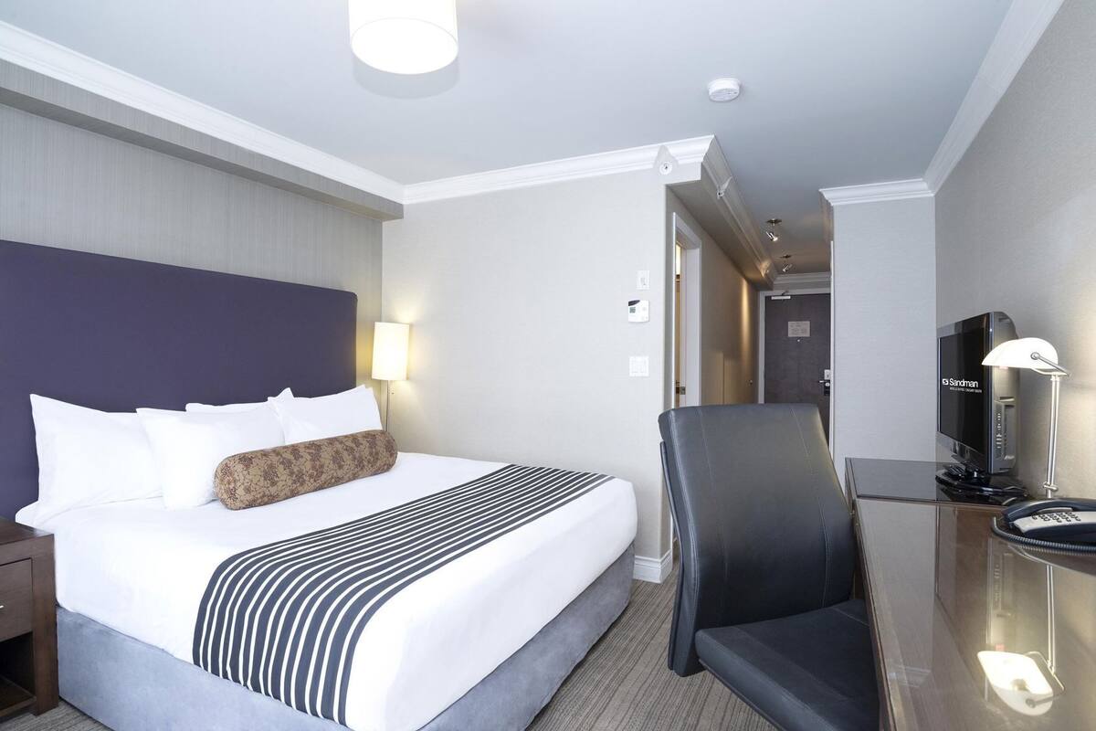 A hotel room with a bed, a desk with a chair, a television, and a lamp.