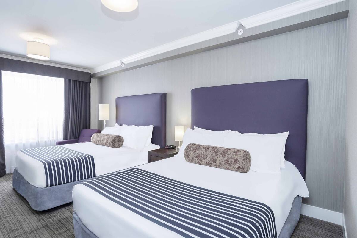 A hotel room with two beds, a large window, and a carpeted floor.