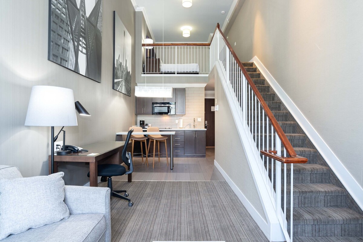 Una habitación de hotel moderna con kitchenette, un comedor y una escalera.