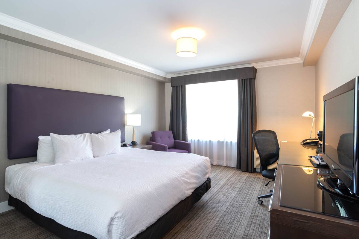 A hotel room with a large bed, a desk with a computer, a chair, and a television.