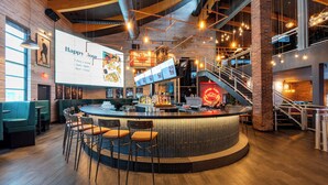 Un área de bar moderna con mostrador, taburetes y una pantalla de menú.