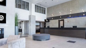 A modern lobby with a reception desk, seating area, and large windows.