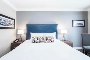 Una habitación de hotel con una cama grande, dos mesitas de noche con lámparas, una silla y obras de arte en las paredes.